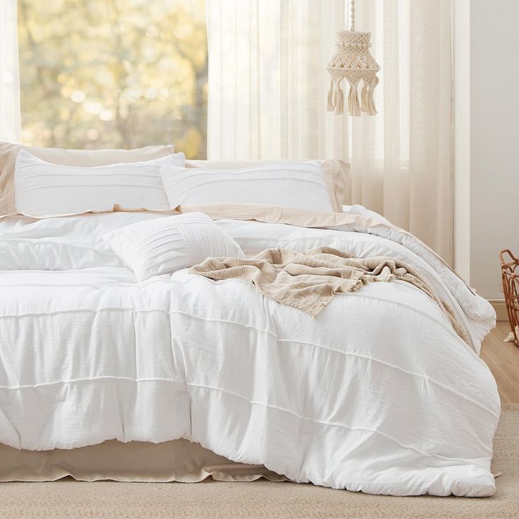 an unmade bed with white sheets and pillows in a room next to a window