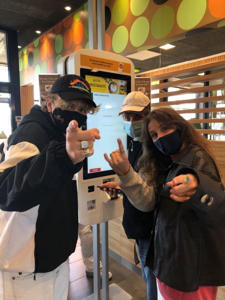 two people wearing face masks are standing in front of a kiosk with their hands up