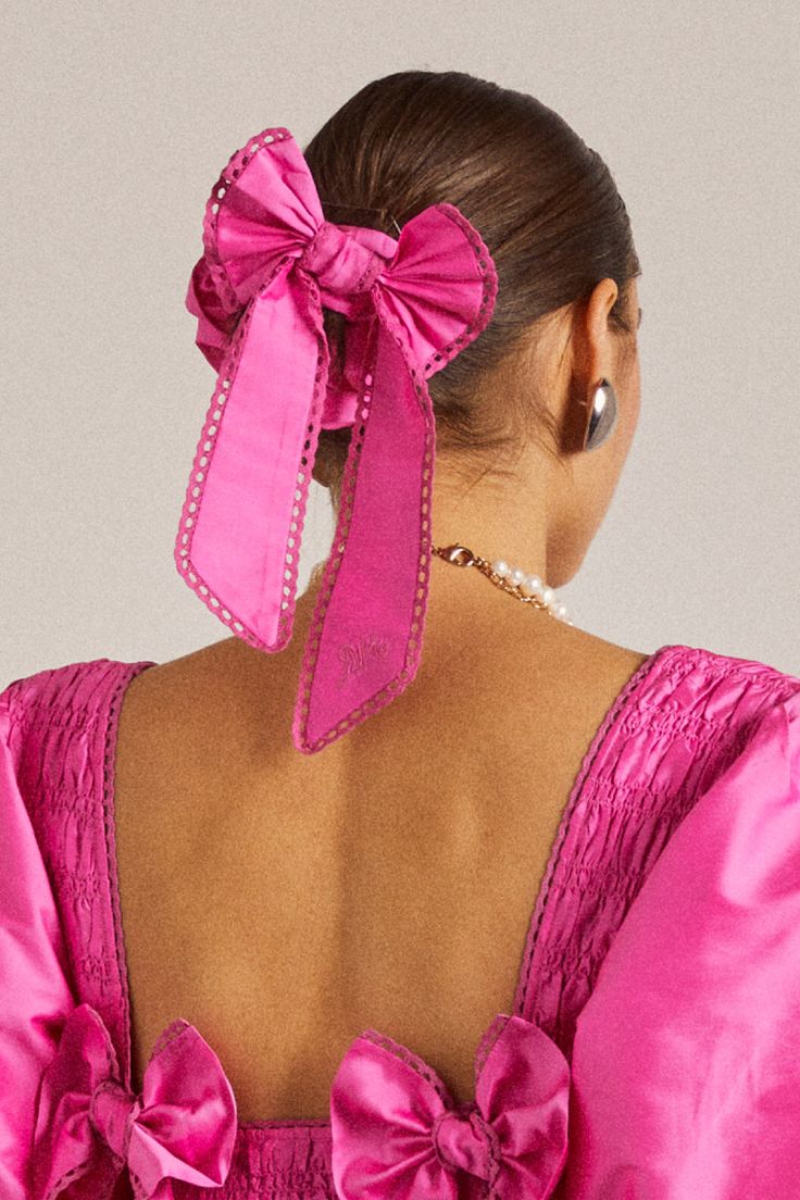 a woman wearing a pink dress with a large bow in her hair and back to the camera