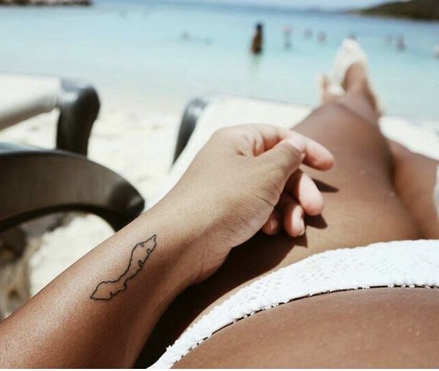 a woman laying on top of a beach next to the ocean with a tattoo on her arm