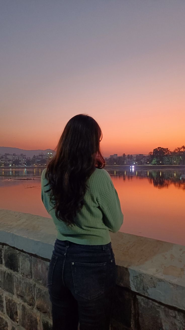 a woman standing next to a brick wall looking at the water