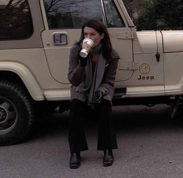 a woman drinking from a cup in front of a jeep