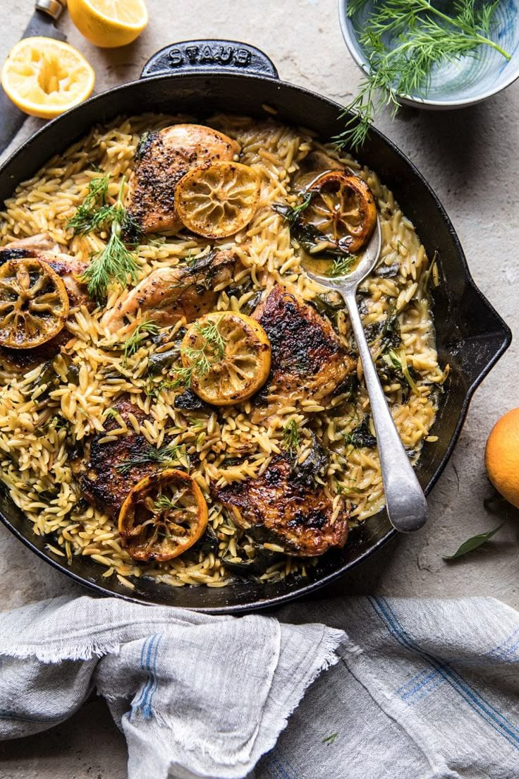 a skillet filled with chicken and rice next to lemons, herbs and spices