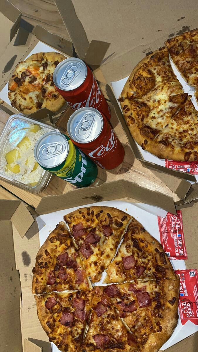 two pizzas and cans of soda sitting on top of a cardboard box next to each other