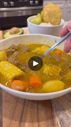 a bowl of soup with corn, carrots and potatoes in it on a wooden table