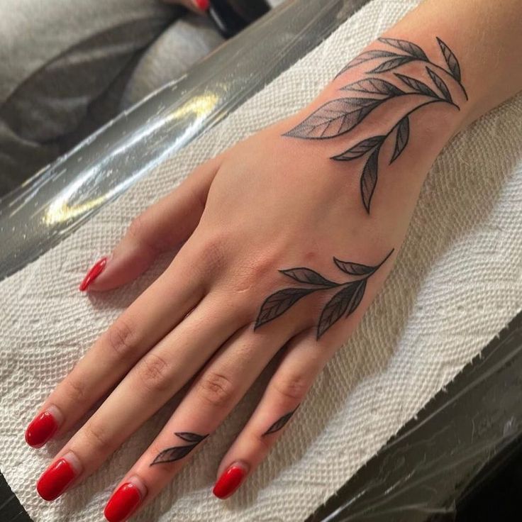 a woman's hand with black leaves on it and red nail polish varing