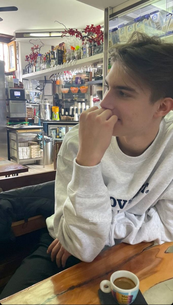 a young man sitting at a table with a cup of coffee in front of him