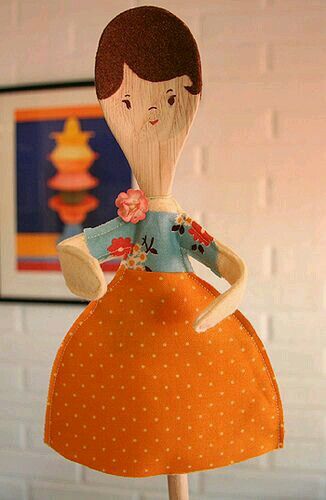 a wooden doll with an orange dress and polka dots on it's body, standing in front of a white brick wall