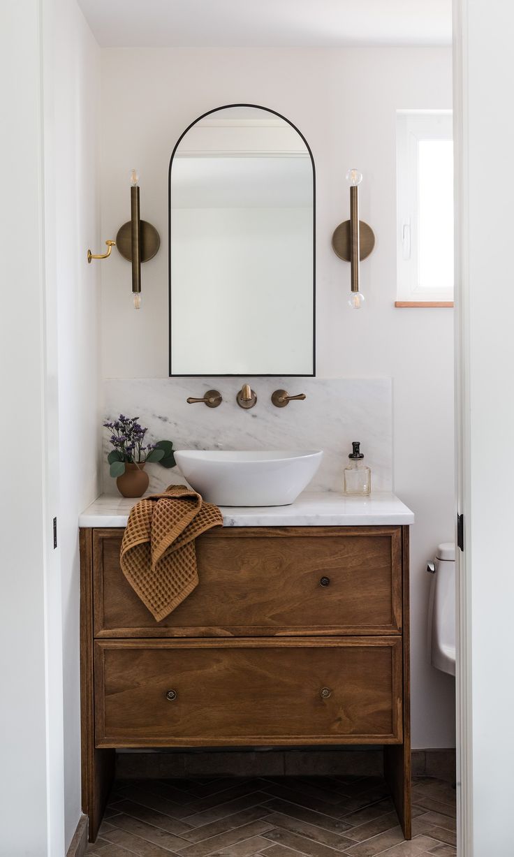 a white sink sitting under a mirror next to a wooden cabinet with a towel on it