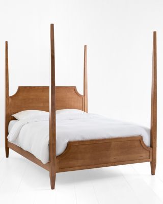 a wooden bed frame with white sheets and pillows on top of it, against a white wall