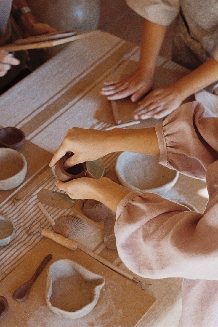 two people are making bowls and spoons on a table with wooden utensils