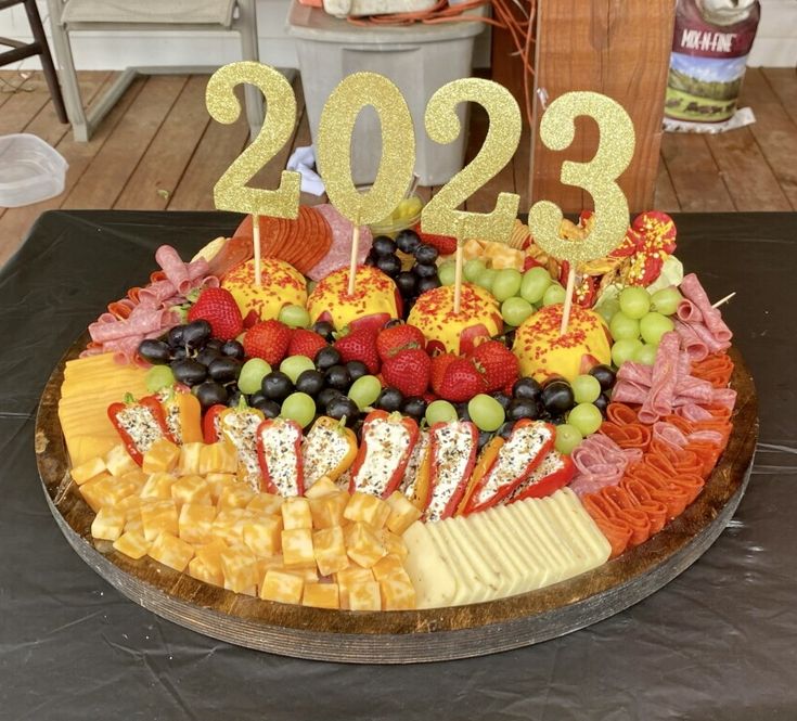 a platter filled with fruit and cheese on top of a wooden table next to a number sign