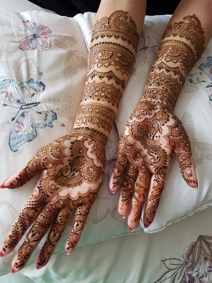 two hands with henna tattoos on them sitting on top of a white bed sheet