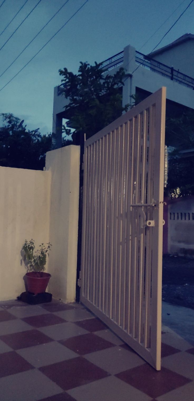 an open gate with a potted plant on the floor in front of it at night