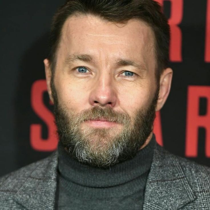 a close up of a person wearing a suit and turtle neck sweater, looking at the camera