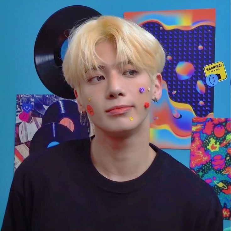 a young man with blonde hair and piercings on his face in front of a blue wall