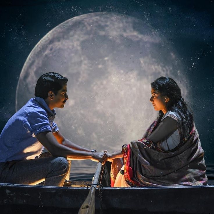 a man and woman sitting on top of a boat in front of a full moon