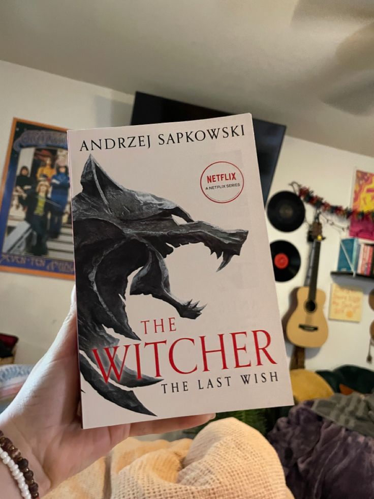 a person holding up a book about the witch in front of a room full of guitars