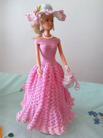 a crocheted doll in a pink dress and hat on a white tablecloth