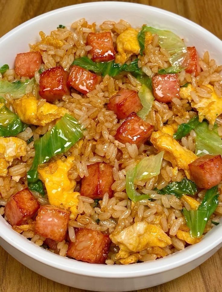 a white bowl filled with rice, meat and veggies on top of a wooden table