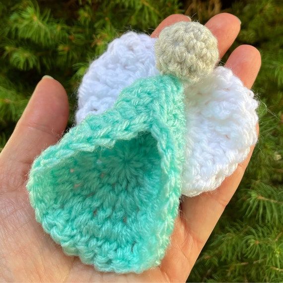 two crocheted angel ornaments are held in someone's hand with pine needles