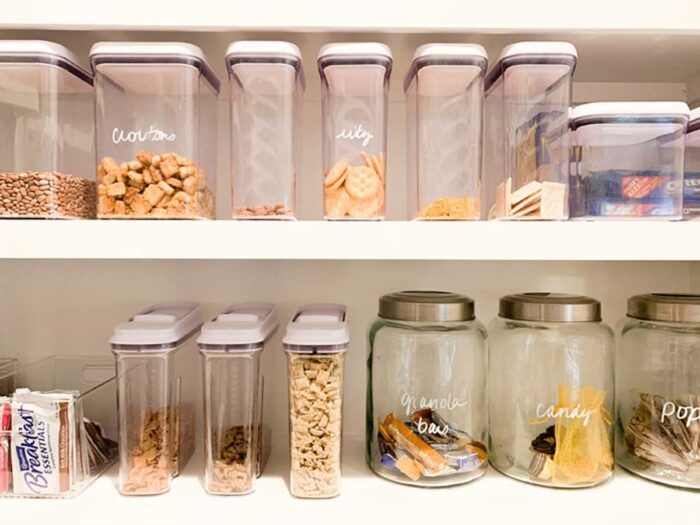 an organized pantry with glass containers and food items on the shelves, including cookies, crackers, cereals, candy bars