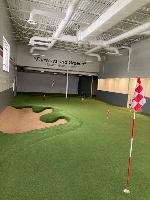 an indoor golf course with green grass and red and white flags