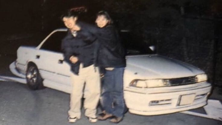 two people standing next to a white car