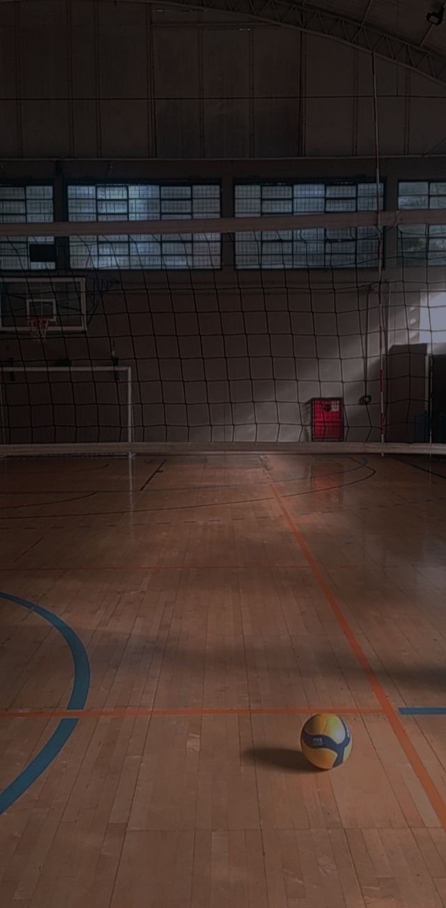 a yellow ball sitting on top of a hard wood floor next to a volleyball net