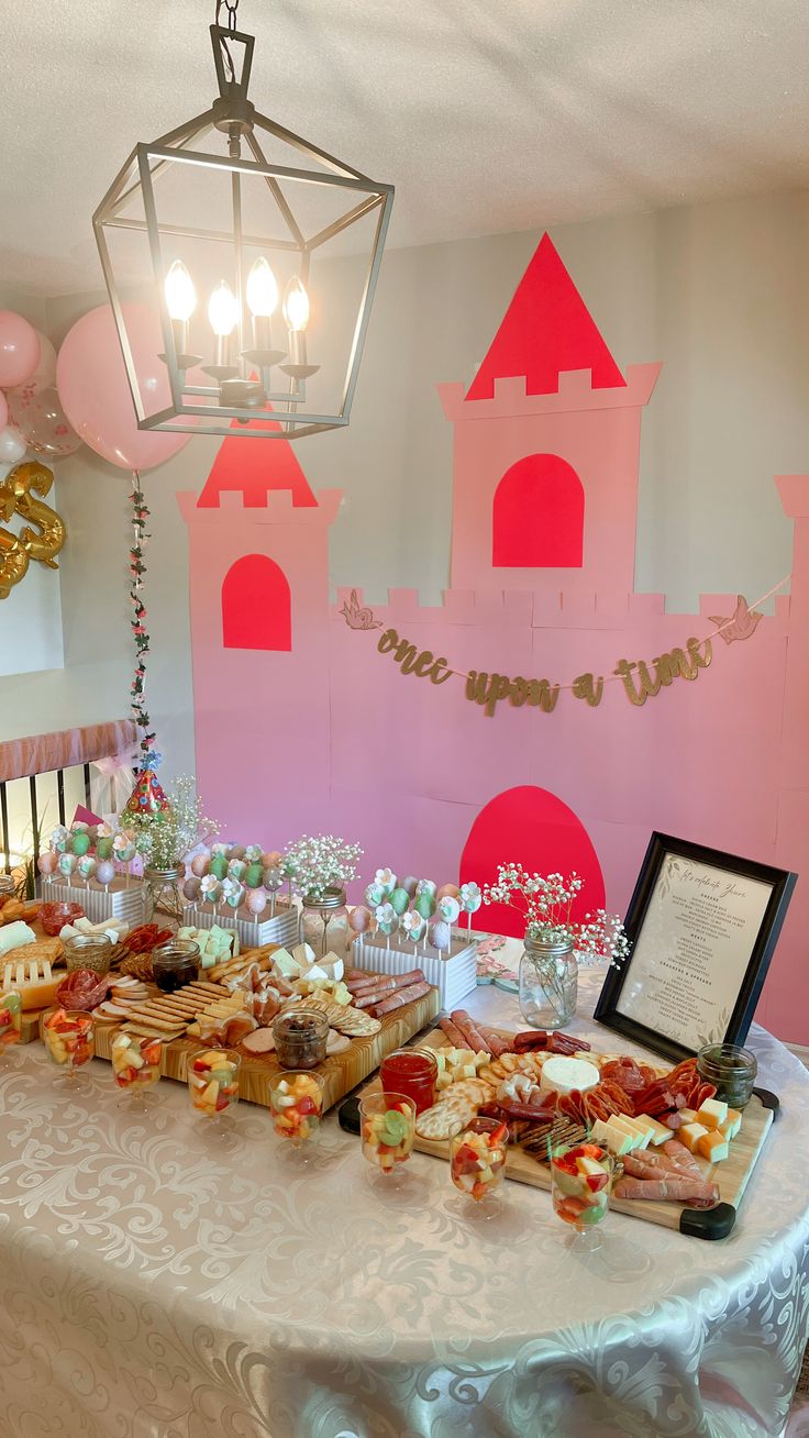 a table topped with lots of food next to a pink castle wall and light fixture