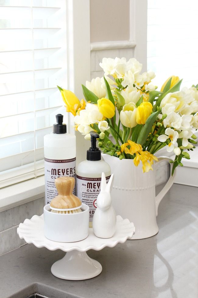 a white pitcher filled with yellow and white flowers next to a bottle of lotion