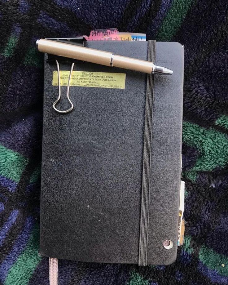 a black notebook with a pen on top of it sitting on a purple and green blanket