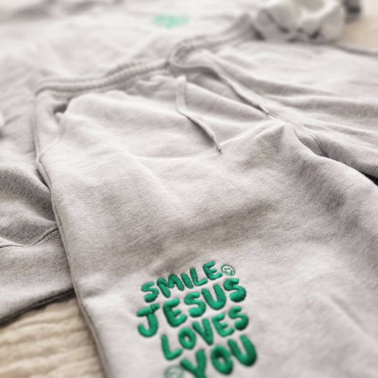 Smile Jesus Loves You Set. Introducing our first set! The Smile Jesus Loves You set :) Share your faith with the most comfy set. Including emerald green embroidery featured on the leg of the shorts and the left chest. The pieces of the set can be purchased separately (Crew only or shorts only) OR together. See info on each piece below Sweatshirt Info: * 50% cotton, 50% polyester * Pre-shrunk * Classic fit * 1x1 athletic rib knit collar with spandex * Air-jet spun yarn with a soft feel and reduce Christian Merch Aesthetic, Christian Drip, Scripture Clothing, Jesus Apparel, Jesus Clothing, Christian Accessories, Christian Crewneck, Letter Designs, Jesus Clothes