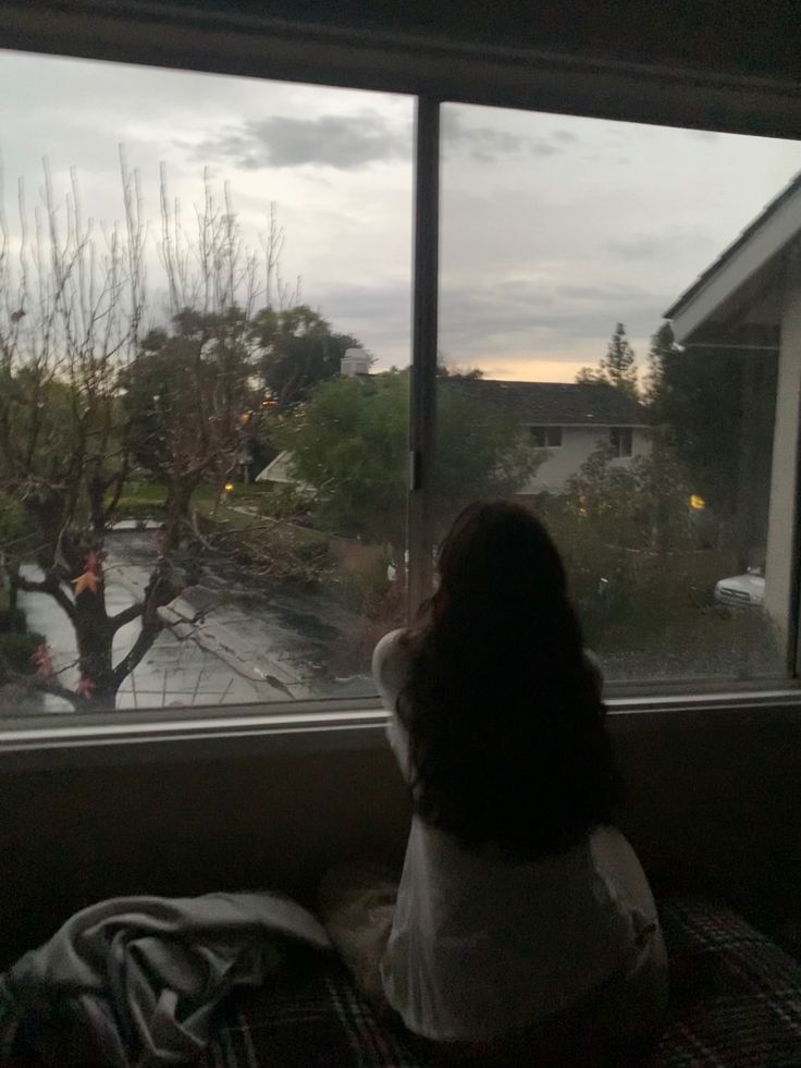 a woman sitting in front of a window looking out at the street outside her house