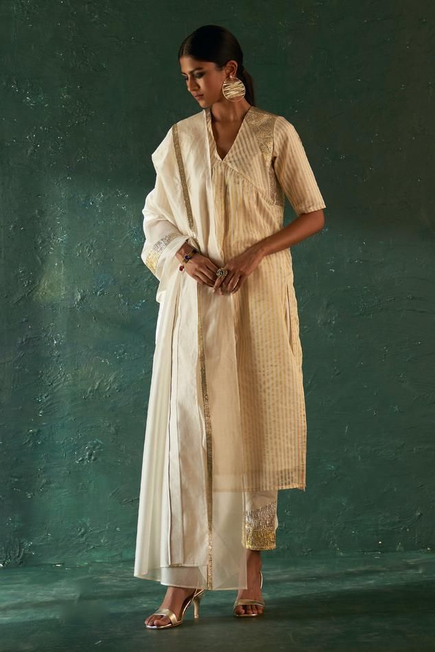 Off-white kurta with striped woven motifs and gota embellishment on shoulders. Paired with gota border embellished pant and dupatta.
Components: 3
Pattern: Woven, Embellished
Type Of Work: Striped, gota
Neckline: V neck
Sleeve Type: Half sleeves
Fabric: Kurta: Silk Tissue, Lining: Cotton, Pant: Poplin, Dupatta: Organza
Color: Off White
Other Details: 
Length:
Kurta: 48 inches
Pant: 37 inches
Dupatta Length: 90 inches
Dupatta Width: 30 inches
Occasion: Puja - Aza Fashions Striped Kurta, Tissue Dupatta, Nida Azwer, Floral Print Sarees, Geometric Texture, Dhoti Pants, White Kurta, Geometric Textures, Straight Kurta