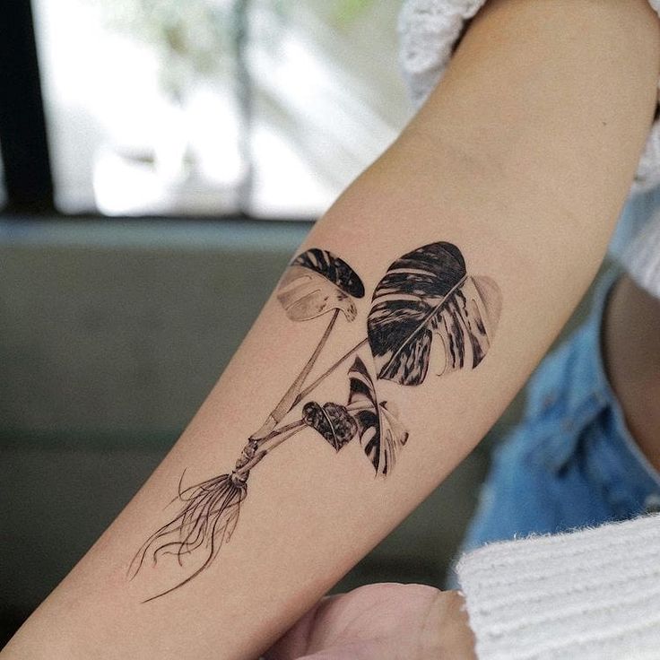 a woman's arm with an inked flower and leaf tattoo on the left forearm