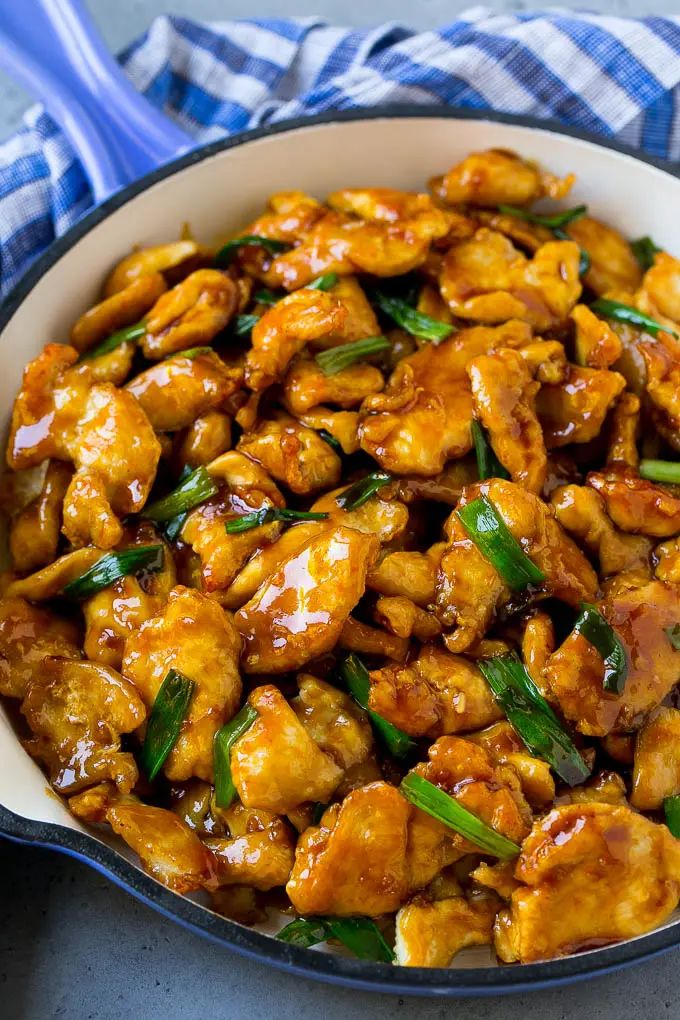 chicken with sauce and green onions in a white bowl on a blue checkered table cloth