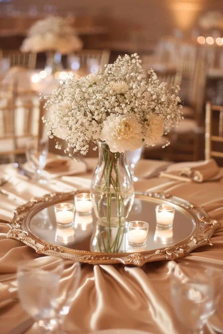 a vase filled with white flowers sitting on top of a table covered in gold cloth