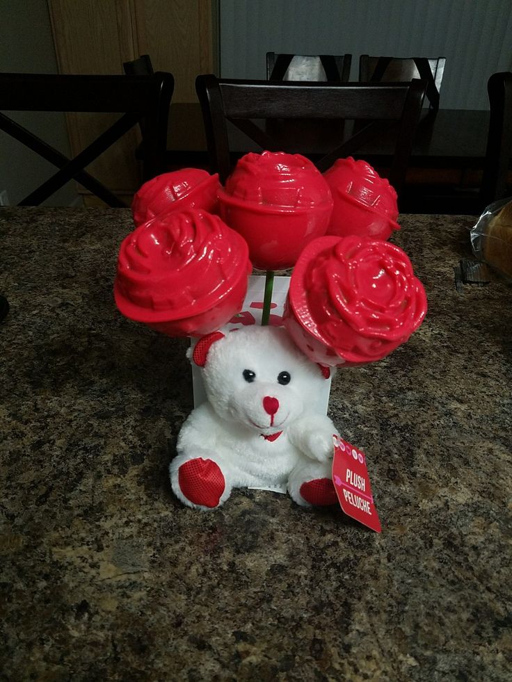 a white teddy bear sitting on top of a counter next to some red roses in a vase