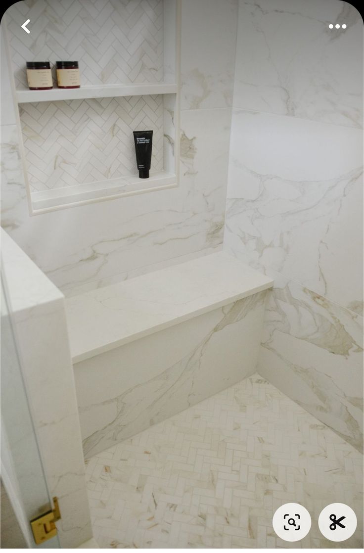 a bathroom with white marble walls and flooring next to a shelf on the wall