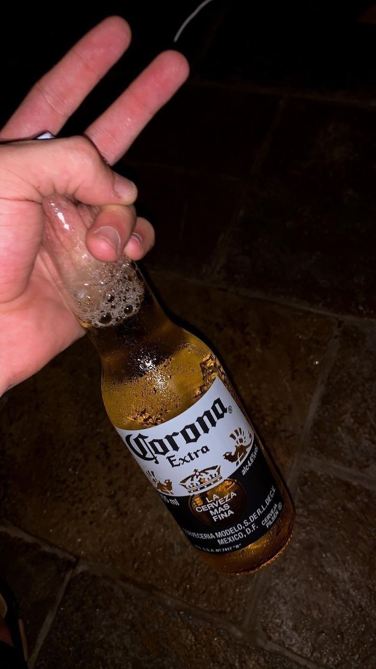 a person holding up a beer bottle with the word corona on it's side