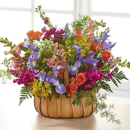 a basket filled with lots of colorful flowers on top of a wooden table next to a window