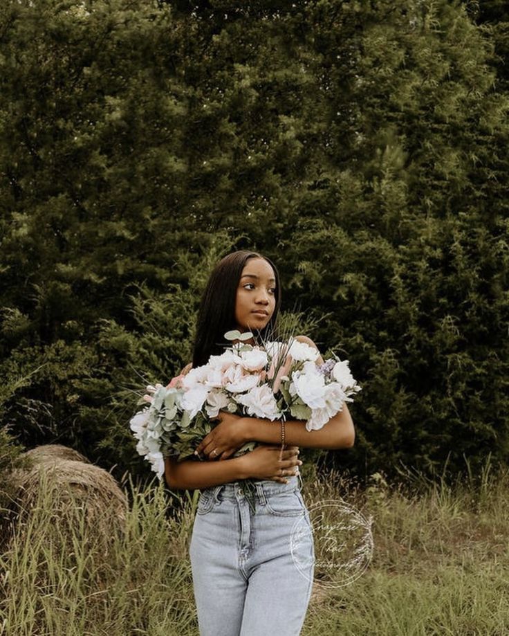 a woman standing in the grass with flowers on her chest and arms around her body