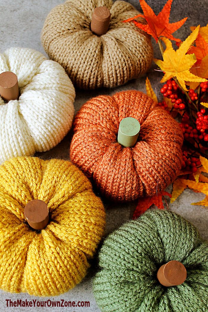 knitted pumpkins with buttons on them sitting next to autumn leaves and fall foliage