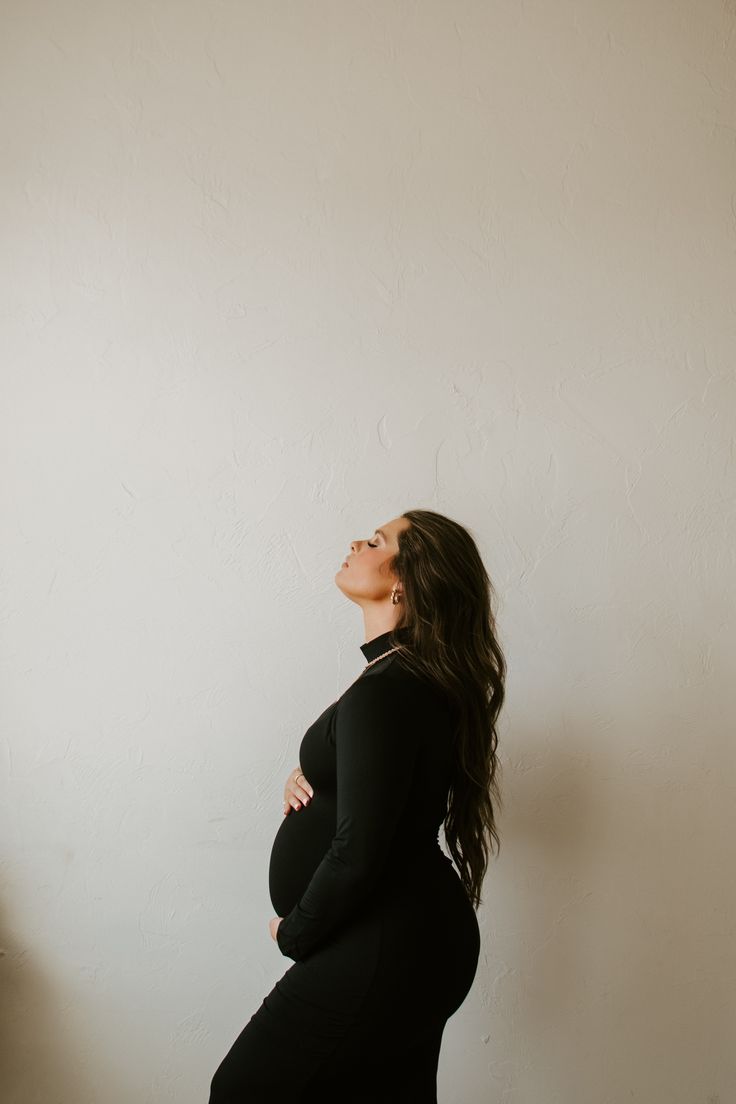 a pregnant woman standing in front of a white wall