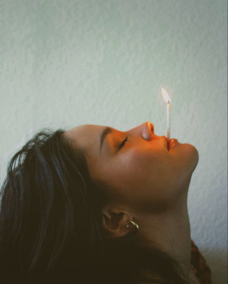 a woman is laying down with a lit candle in her mouth and looking up at the sky