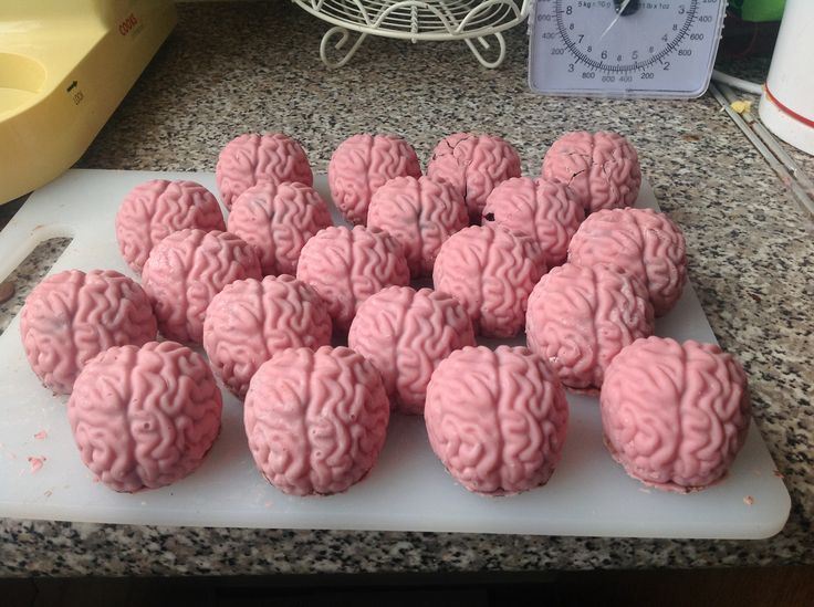 a bunch of pink brain cookies on a cutting board next to a scale with a clock in the background