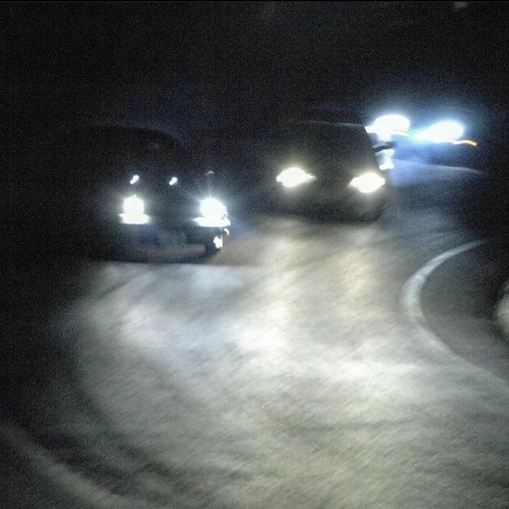 three cars driving down a road at night with headlights on and fog coming from them