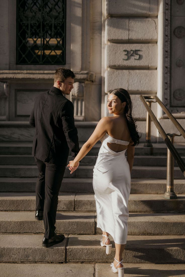 a man and woman holding hands walking up some steps