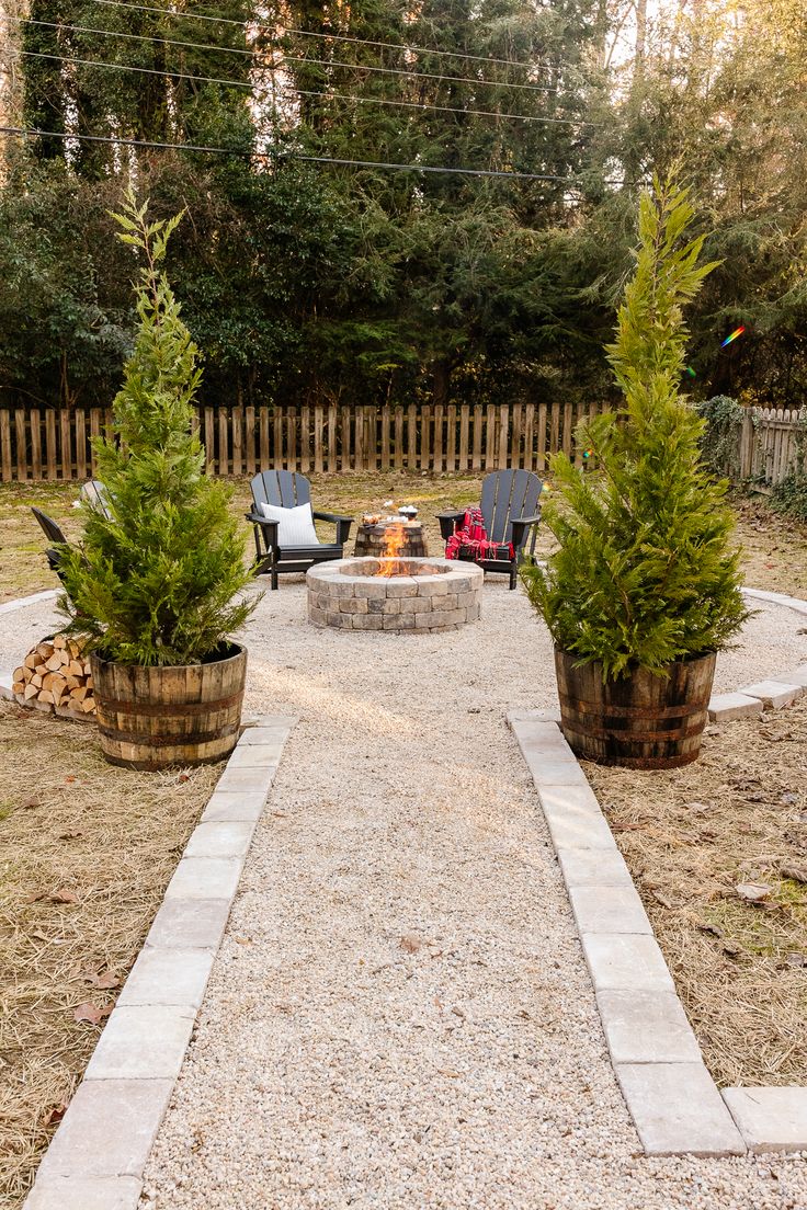 an outdoor fire pit surrounded by two large planters and three chairs in the background